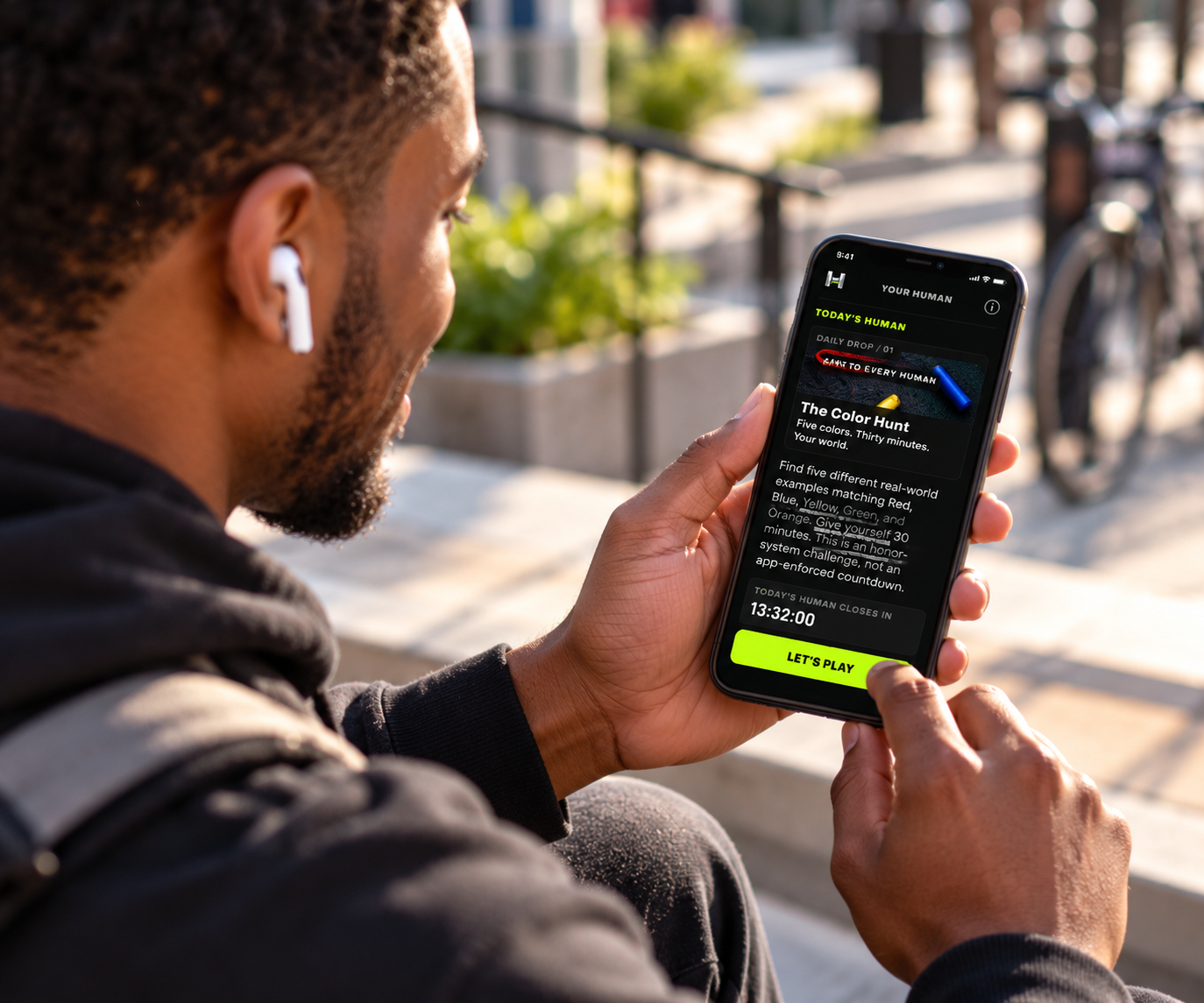 A man on a sunny city walk opens HUMAN and reads today's surprise challenge, The Color Hunt, on his phone